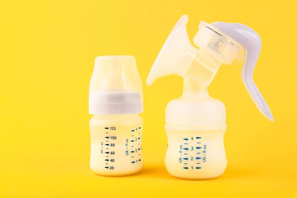 White plastic baby bottle with pacifier,breast pump rich in baby food, on yellow background. Copy space.