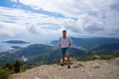 Adriyatik Denizi ve Karadağ 'ın Budva kentinin muhteşem manzaralı bir dağ zirvesinin kenarında poz veren beyaz adam.