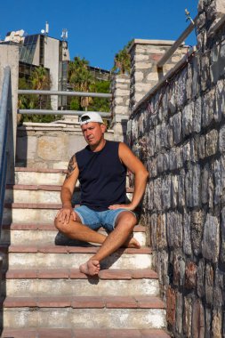 Kolunda dövmesi olan güçlü ve yakışıklı bir genç adam eski toprak setinde poz veriyor. Tivat, Karadağ.