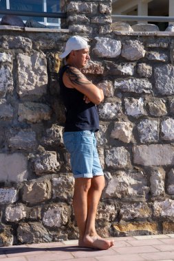 Kolunda dövmesi olan güçlü ve yakışıklı bir genç adam eski toprak setinde poz veriyor. Tivat, Karadağ.