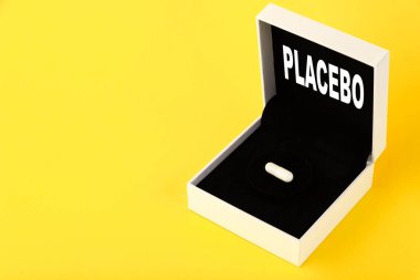 Placebo, metin bir hediye kutusuna yazılmış. Sarı arka planda beyaz kapsüllü bir hediye. Boşluğu kopyala