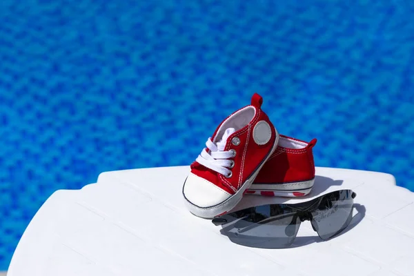 Zonnebrillen Rode Kindergymschoenen Liggen Een Witte Chaise Lounge Tegen Achtergrond — Stockfoto