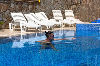 Mavi suyla havuzda genç yakışıklı bir adam güneşli bir günde dinleniyor..