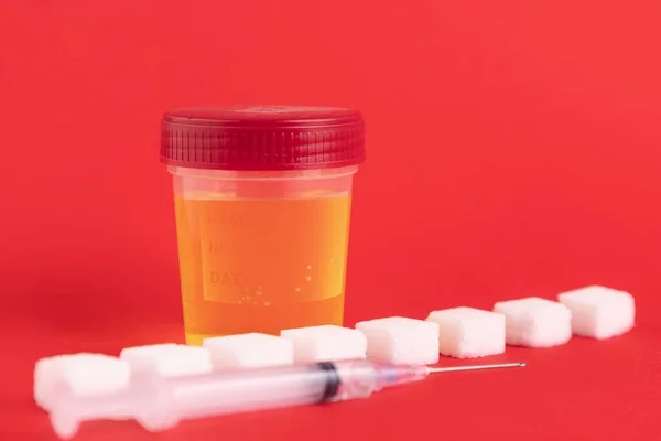General urine test in a medical container and white sugar cubes with a syringe. Copy space. Selective focus.