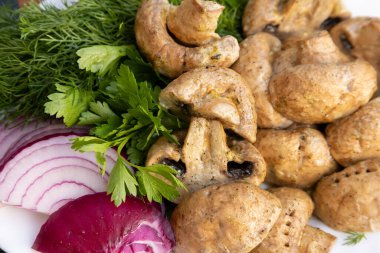 Beyaz bir tabakta duran ızgara şampiyon mantarları, otlar ve kırmızı soğanlarla süslenmiş. Seçici odak.