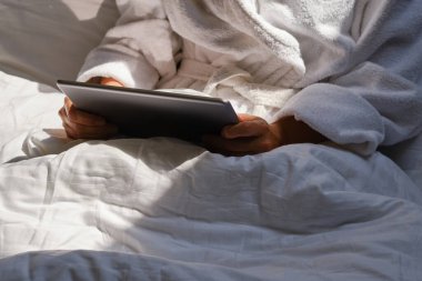 Kadın tableti elinde tutuyor. Yatakta rahat. Evde sabah online aktiviteleri. Mobil cihazda film ve TV programları izliyordum. Sosyal medya bağımlılığı. Evde çalış, serbest çalış. Yaşam tarzında teknoloji