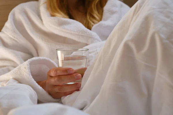 一个睡在床上的女孩旁边的一杯水 早晨快乐 穿着睡衣的女人健康的生活 健康的生活 适当的营养 饮用水 早上与水 亚麻布上的阳光 — 图库照片