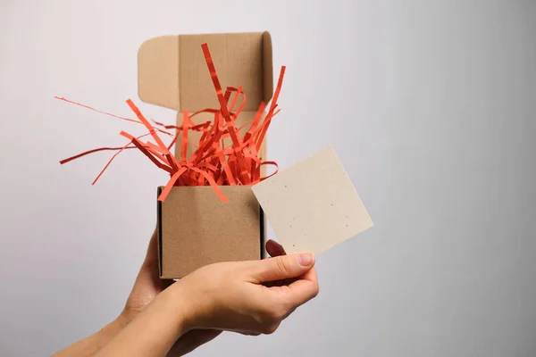 女性は郵便はがきを手に驚きの箱を持っています 美しいお祝いのパッケージ 休日プレゼントを開く時間 紙のギフトボックス 招待状とおめでとう 郵便はがきの空白スペース — ストック写真