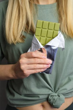 Bir kızın elinde kibritli çikolata. Yeşil çikolata çubuğu. Lezzetli tatlı. Kakao ve Japon yeşil çay şekeri. Sağlıklı vejetaryen yemeği. Organik yiyecekler. Çikolata yakın plan.