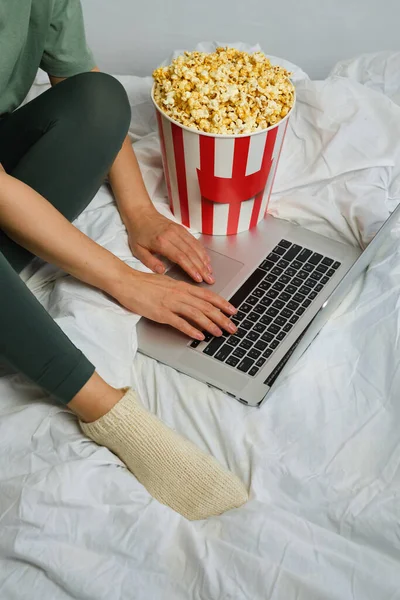 一个准备在床上用笔记本电脑看电影的小女孩手里拿着爆米花桶 表演时间到了吃美味的甜零食 在家里看新电影 卧房休息和娱乐 — 图库照片