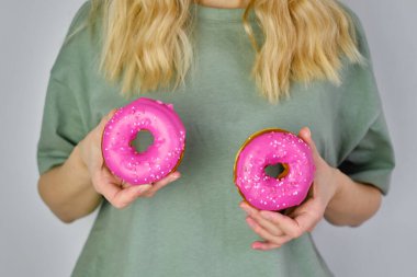 Bir kızın ellerinde renkli çörekler. Lezzetli tatlı Amerikan tatlısı. Popüler hamur işleri. Parlak şeker kaplı donut yakın plan. Elinde çöreklerle poz veren bir kadın. Fast food