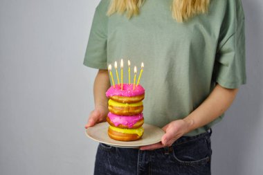 Kızın ellerinde mumlar olan pembe çörekler. Lezzetli pastalarla doğum günü. Açık şeker jöleli çörek yakın plan. Bayramlık tatlı Amerikan tatlısı. Popüler hamur işleri