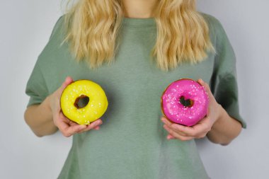 Bir kızın ellerinde renkli çörekler. Lezzetli tatlı Amerikan tatlısı. Popüler hamur işleri. Parlak şeker kaplı donut yakın plan. Elinde çöreklerle poz veren bir kadın. Fast food