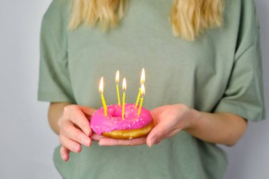 Kızın ellerinde mumlar olan pembe çörekler. Lezzetli pastalarla doğum günü. Açık şeker jöleli çörek yakın plan. Bayramlık tatlı Amerikan tatlısı. Popüler hamur işleri