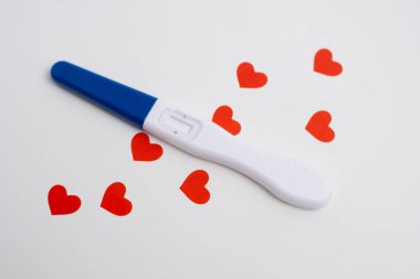 Beyaz zemin üzerinde kırmızı kalpler konfetisi olan pozitif hamilelik testi