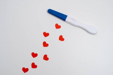 Beyaz zemin üzerinde kırmızı kalpler konfetisi olan pozitif hamilelik testi