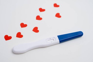 Beyaz zemin üzerinde kırmızı kalpler konfetisi olan pozitif hamilelik testi