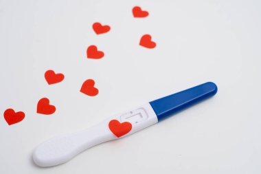 Beyaz zemin üzerinde kırmızı kalpler konfetisi olan pozitif hamilelik testi