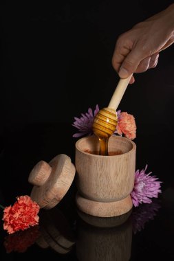 Ballı ahşap kase, bal damlatıyor, çiçekleri siyah arka planda.