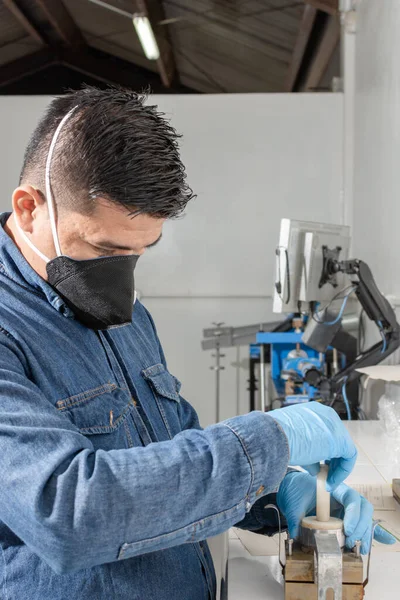 Latin adamın koruyucu maske ve mavi lateks eldiven kullanarak jeolojik test makinesini kalibre ettiği yakın plan.