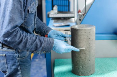 Beton silindiri ölçen mavi lateks eldivenli erkek sanayi işçisi elleri