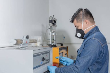 Endüstriyel işçi koruyucu maske ve mavi lateks eldiven kullanarak jeolojik test makinesini kalibre ediyor.