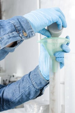 Mavi lateks eldivenli endüstriyel işçi elleri test pipetine kum döküyor.