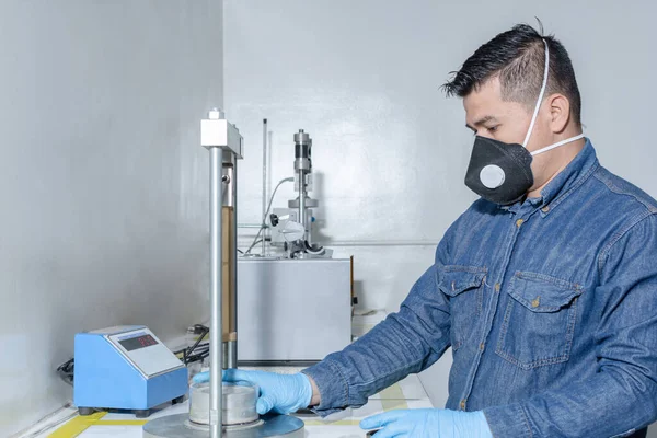 Endüstriyel işçi koruyucu maske ve mavi lateks eldiven kullanarak jeolojik test makinesini kalibre ediyor.