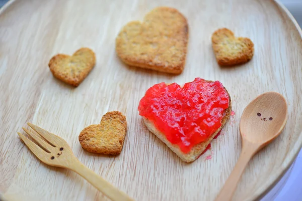 Brot schneiden und rote Erdbeermarmelade in Herz- und Holzform Stockbild