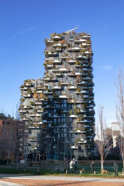 Milan, İtalya - 10 Aralık 2021: Bosco Verticale kulelerinin balkonlarında ağaçlar ve ön planda çitli bir köpeğin koştuğu bir park manzarası.