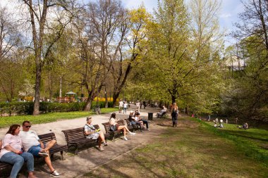 Vilnius, Litvanya - 21 Nisan 2025: Bernardine Garden, Vilnius 'ta güneşli bir bahar gününün tadını çıkaran insanlar, çiçek açan ağaçlarıyla Vilnia nehrinin çimlerinde dinleniyorlar..