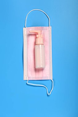 Mavi arka planda pembe tıbbi maske ve dezenfektan.