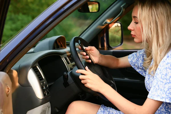 Young woman talking on a cell phone while sitting in the car in the drivers seat. Attractive blonde female student — Stock Photo, Image