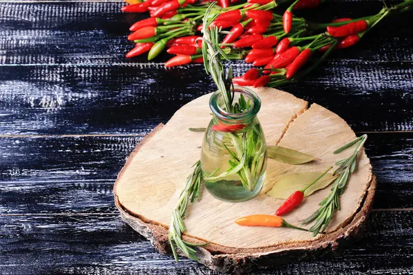 Olive oil spiced with hot pepper rosemary on a black wooden background — Stock Photo, Image