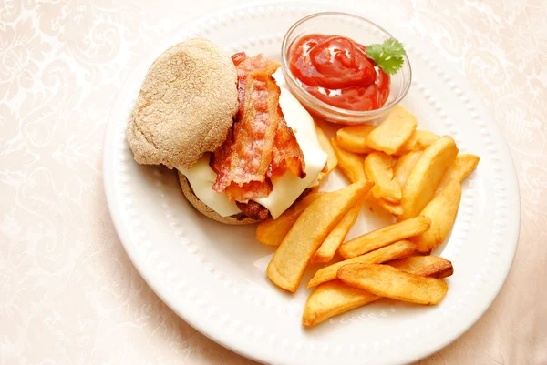 Чизбургер с беконом, подаваемый на пшеничном английском кексе с жареной картошкой — стоковое фото