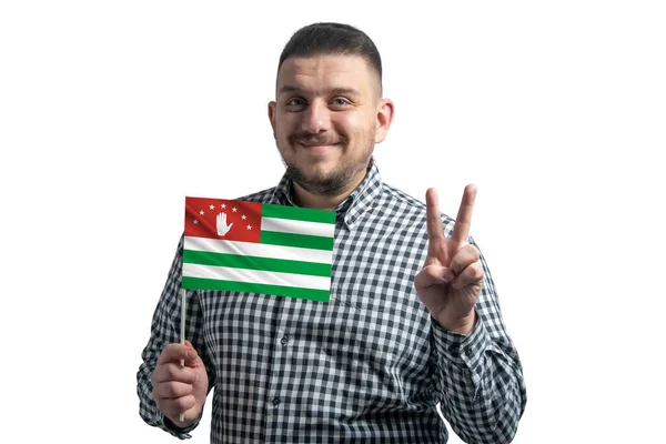 Homem branco segurando uma bandeira da Abcásia e mostra dois dedos isolados em um fundo branco — Fotografia de Stock