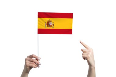Güzel bir dişi el, beyaz arka planda izole edilmiş diğer elinin parmağını gösterdiği bir İspanya bayrağını tutuyor..