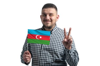 Azerbaycan bayrağı taşıyan beyaz bir adam beyaz arka planda iki parmak gösteriyor..
