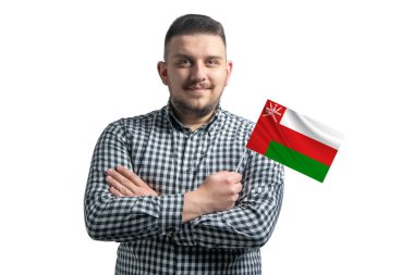 Beyaz adam Umman 'ın bayrağını tutuyor. Beyaz bir arka planda kollarını kavuşturup gülümsüyor..