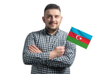 Beyaz adam Azerbaycan bayrağı taşıyor. Beyaz bir arka planda kollarını kavuşturup gülümsüyor..