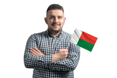 Madagaskar 'ın bayrağını tutan beyaz bir adam beyaz bir arka planda kollarını kavuşturmuş kendinden emin bir şekilde gülümsüyor..