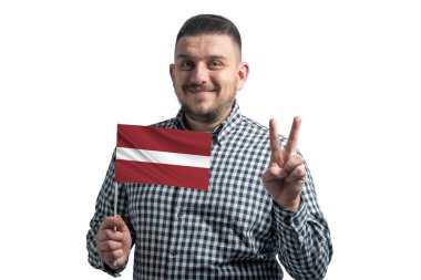 Beyaz adam Letonya bayrağını tutuyor ve beyaz arka planda iki parmak gösteriyor..