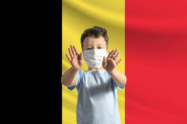 打着比利时国旗背景的戴着防护面具的白人小男孩 用手做一个停车标志 呆在家里比利时 — 图库照片