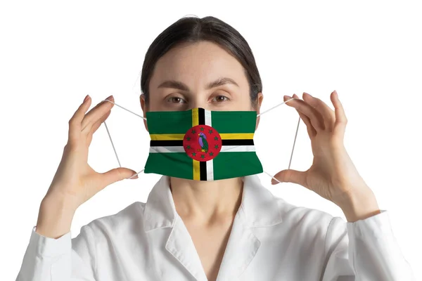 ドミニカの旗を持つ呼吸器医師は白い背景に隔離された医療面マスクに置きます — ストック写真