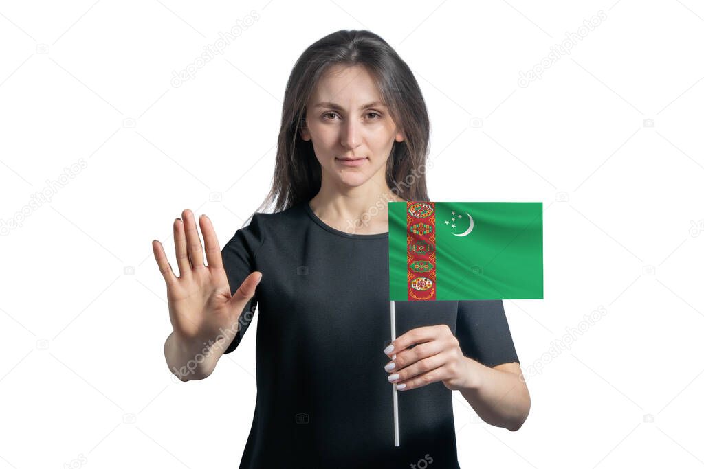 Happy young white woman holding flag of Turkmenistan and with a serious face shows a hand stop sign isolated on a white background.