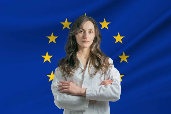 欧洲联盟的医学 在欧盟旗帜的衬托下 身穿军大衣 手挽手站在那里的美丽的女医生 幸福极了 图库图片
