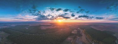 İlkbahar kırsal arazisi sabah güzel yanan gökyüzü ile. Hava görüntüsü. Güneş doğarken çam ormanlarının, tarlaların ve köyün panoramik manzarası. 21 görüntüden 180. Panorama