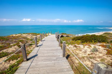 Paredes Panoramik Boardwalk. Güneşli bir günde, kayalık deniz kıyısındaki ahşap merdiven. Sahil Polvoeira, Portekiz