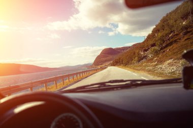 Gün batımında fiyort boyunca dolambaçlı bir yolda araba sürmek.