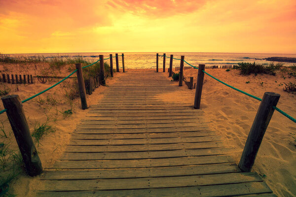 Wooden walkway on the sandy beach at magical sunset light. Beautiful seascape in the evening